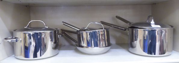 A graduated set of five stainless steel saucepans with lids and a frying pan