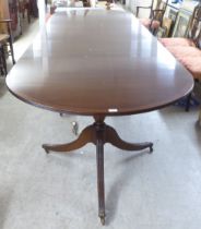 A 20thC reproduction of a Regency crossbanded mahogany triple pedestal dining table with two