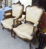A pair of late Victorian style walnut showwood framed open arm salon chairs, upholstered in two tone
