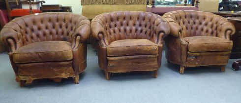 A set of three early/mid 20thC stud and part button upholstered simulated brown hide armchairs,