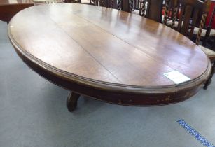 An early 20thC oak pedestal table, the oval planked top raised on a carved C-scroll quadruped