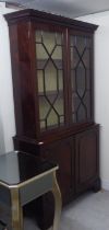 A Regency style two part mahogany cabinet bookcase with a straight cornice, over a pair of