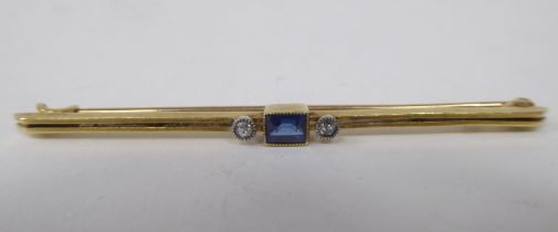 A yellow metal bar brooch, set with a baguette cut sapphire, flanked by two diamonds  stamped 15ct