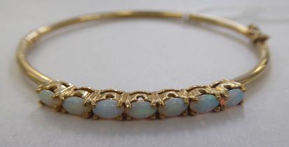 A 9ct gold hinged bangle, set with seven opal cabochons