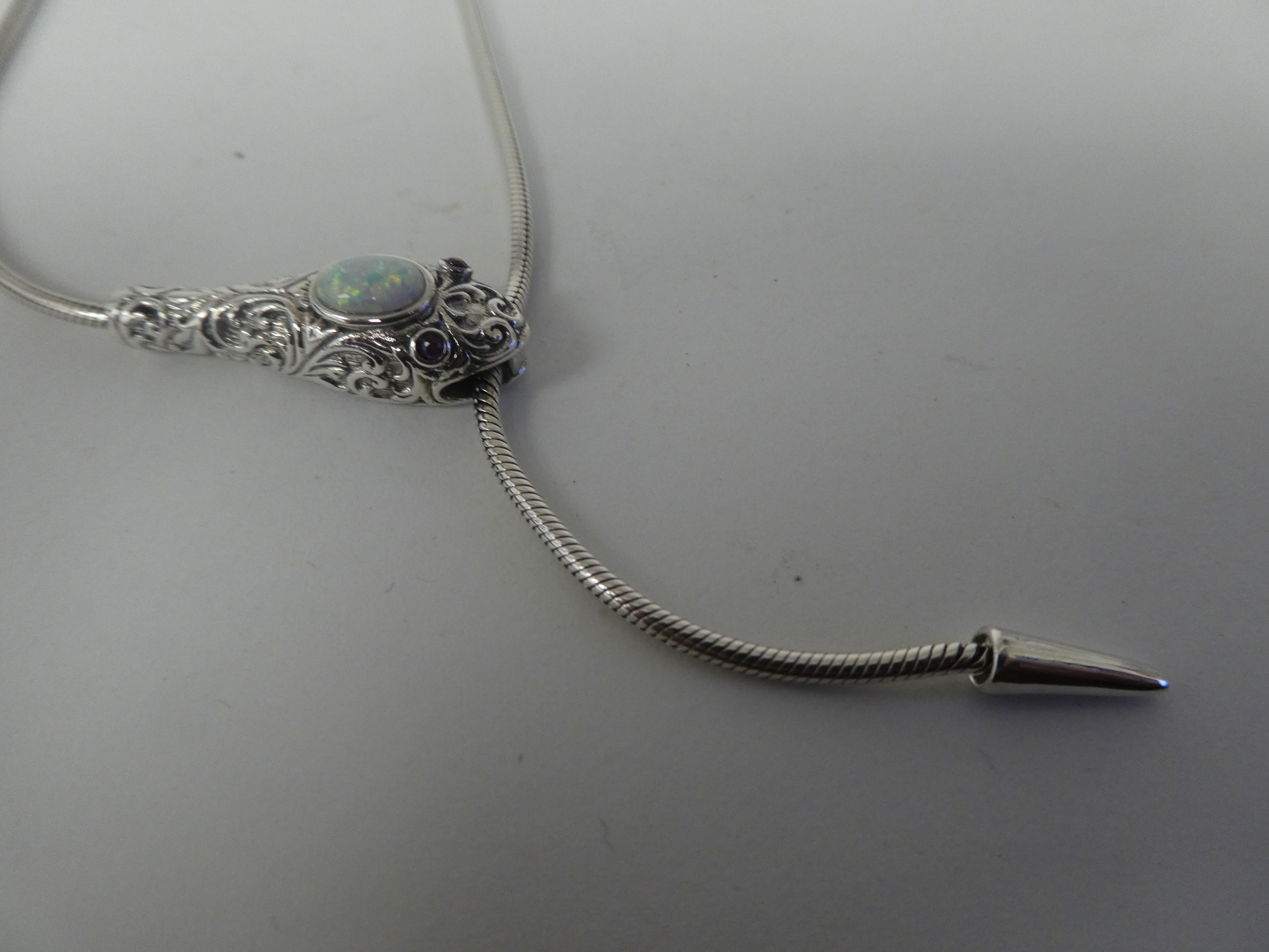 A silver coloured metal, opal set snake necklace with ruby set eyes