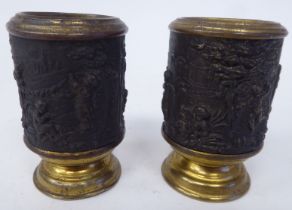 A pair of lacquered brass and tinplate vesta holders, fashioned with embossed scenes of cherubs in