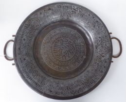 A late 19thC Middle Eastern bi-coloured copper charger with opposing iron loop handles, engraved