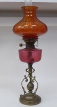 A reproduction of a Victorian style brass oil lamp with a cranberry coloured glass reservoir and