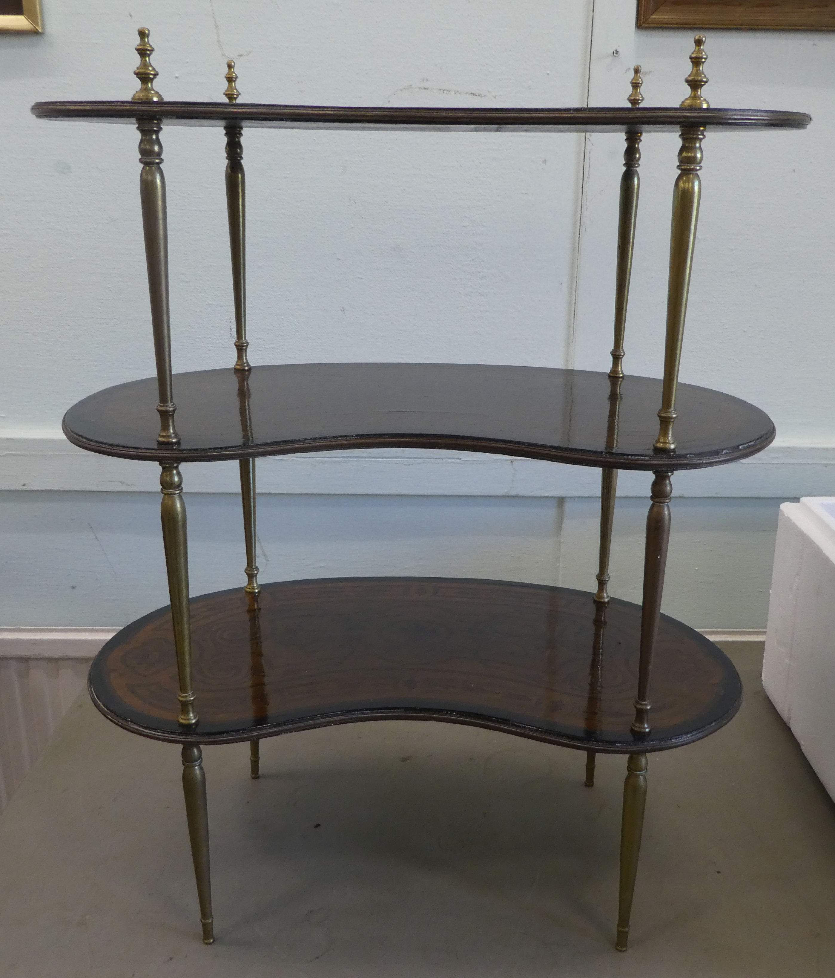 An early 20thC overpainted mahogany kidney shaped three tier whatnot, elevated on tapered, brass