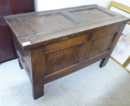 A late 18th/early 19thC panelled oak coffer with straight sides and a hinged lid, raised on block