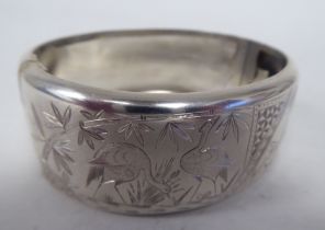 A white metal hinged bracelet, decorated with birds in a wetland setting