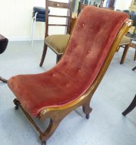 A late 19thC walnut framed nursing chair with a maroon fabric upholstered back and seat, raised on