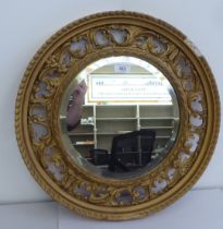 An early 20thC mirror with a bevelled plate within a pierced, gilt gesso swag frame  19"dia