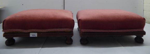 A pair of late Victorian mahogany footstools with maroon fabric upholstered tops, raised on bun feet