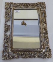 A 19thC mirror, set in a foliate scroll carved wooden and silvered, bead bordered frame  18" x 14"