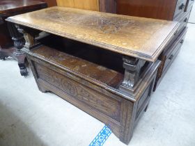 A 1930s oak monks bench with carved arms and a hinged seat, over a panelled front, raised on block