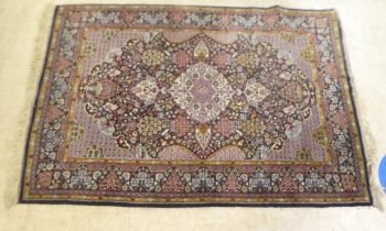 A Persian rug, decorated with a central motif, bordered by stylised designs, on a multi-coloured