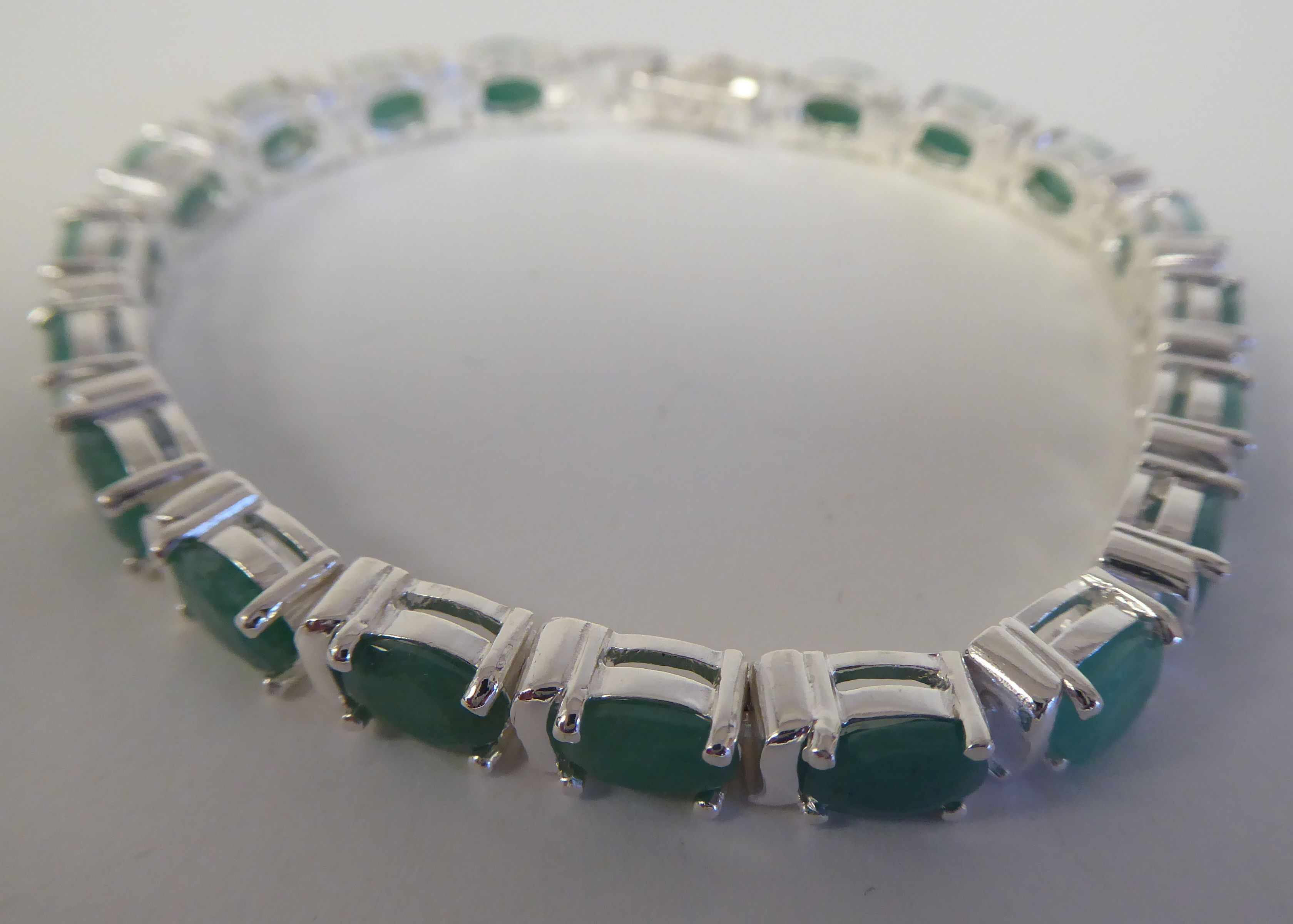 A silver coloured metal, claw set emerald, inline bracelet  stamped 925