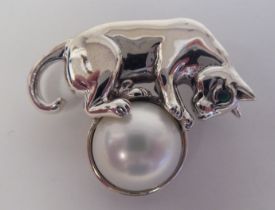 A silver coloured metal brooch, fashioned as a cat, standing on a pearl  stamped Sterling