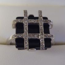 A white gold coloured metal, onyx and diamond set crossover ring