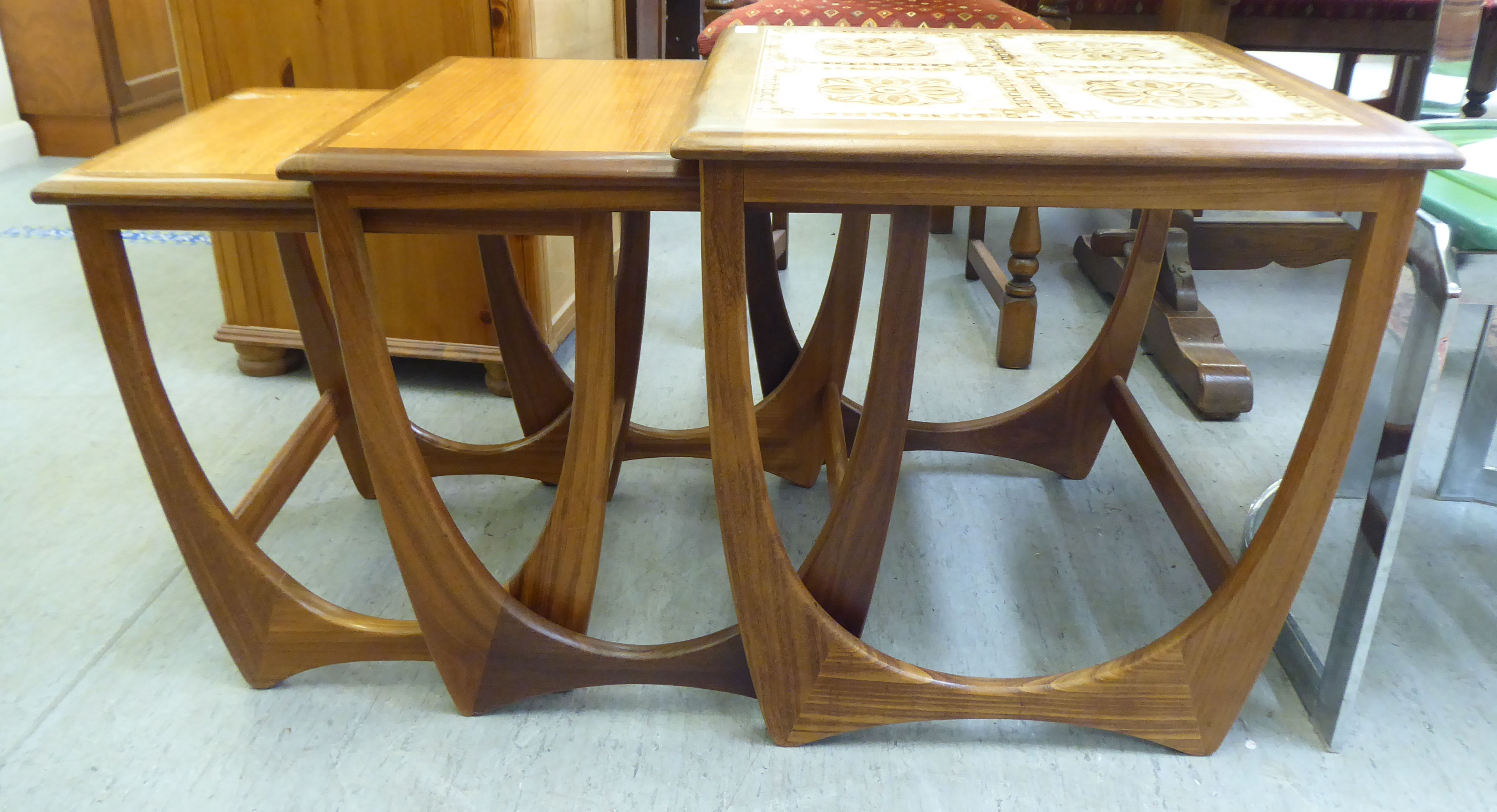 A nesting set of three G-Plan teak occasional tables, the largest top set with tiles, raised on