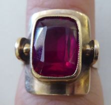 A yellow metal ring, set with a red stone