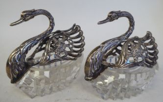A pair of 20thC cut glass and silver coloured metal mounted swan ornaments with folding wings