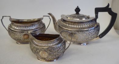 A late Victorian silver three piece tea set of oval form with engraved, chased and demi-reeded