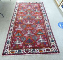 An Afghan rug, decorated with repeating stylised designs, on a mainly red ground  57" x 110"