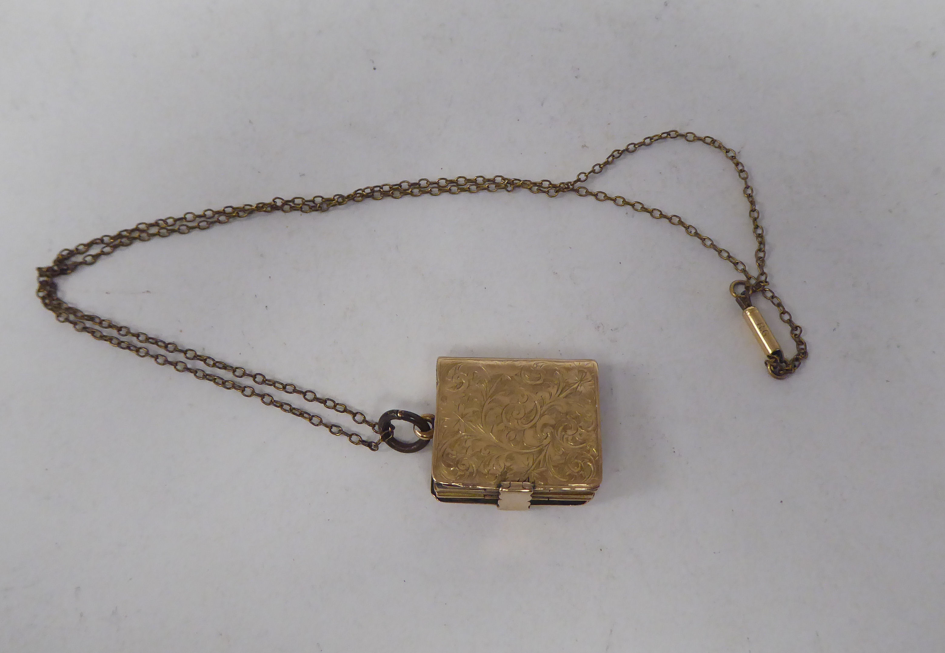 A late Victorian foliate scrolled yellow metal locket, fashioned as a book, on a clasp, revealing