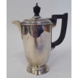 A silver hot water pot of baluster form with a hinged lid, ebonised handle and knop, on a splayed