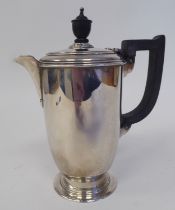 A silver hot water pot of baluster form with a hinged lid, ebonised handle and knop, on a splayed