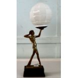 A 1930s Art Deco patinated and gilded table lamp. fashioned as a woman holding a white glass