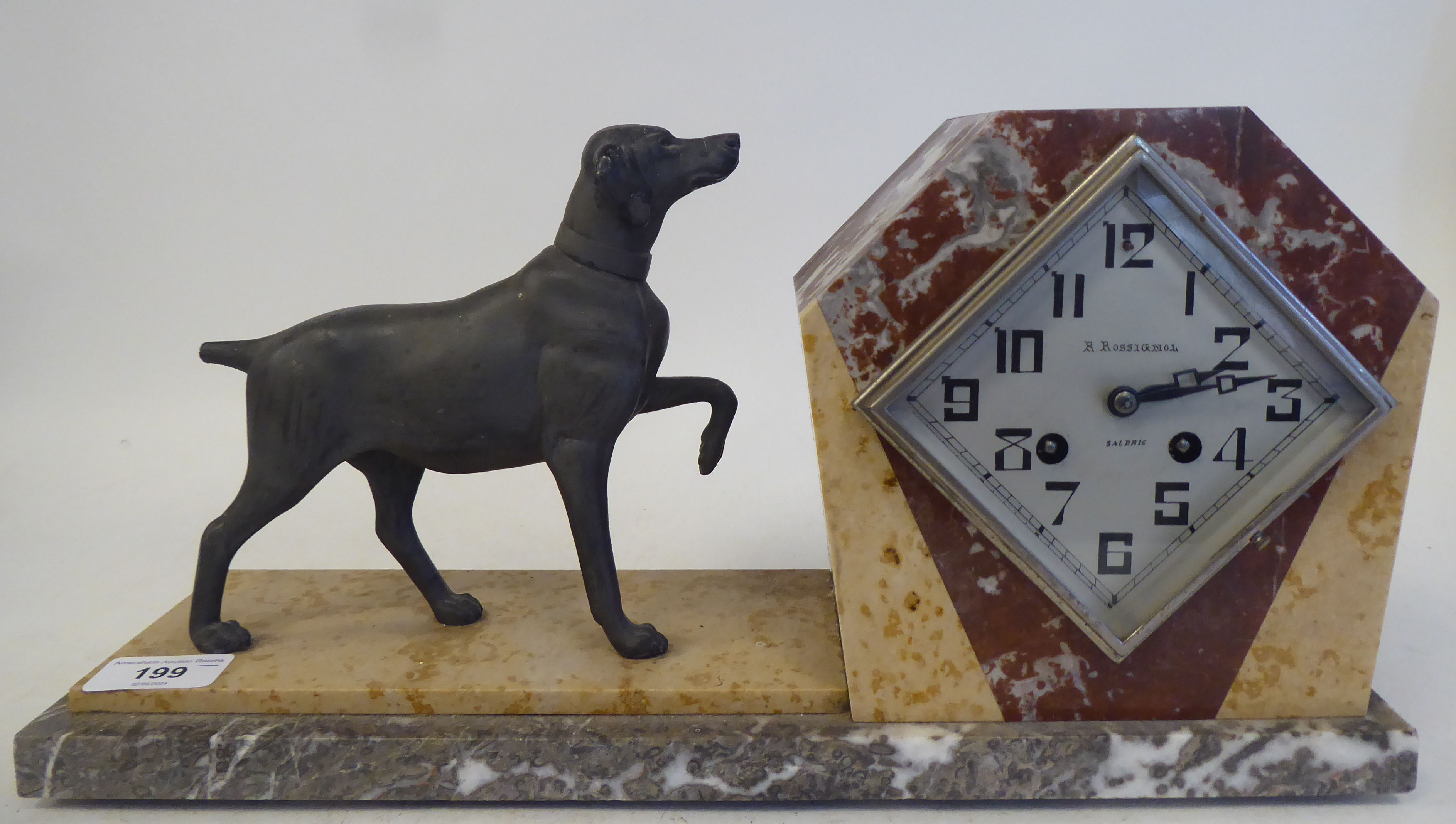 An Art Deco multi-coloured marble cased mantel clock, surmounted by a spelter standing hound; the
