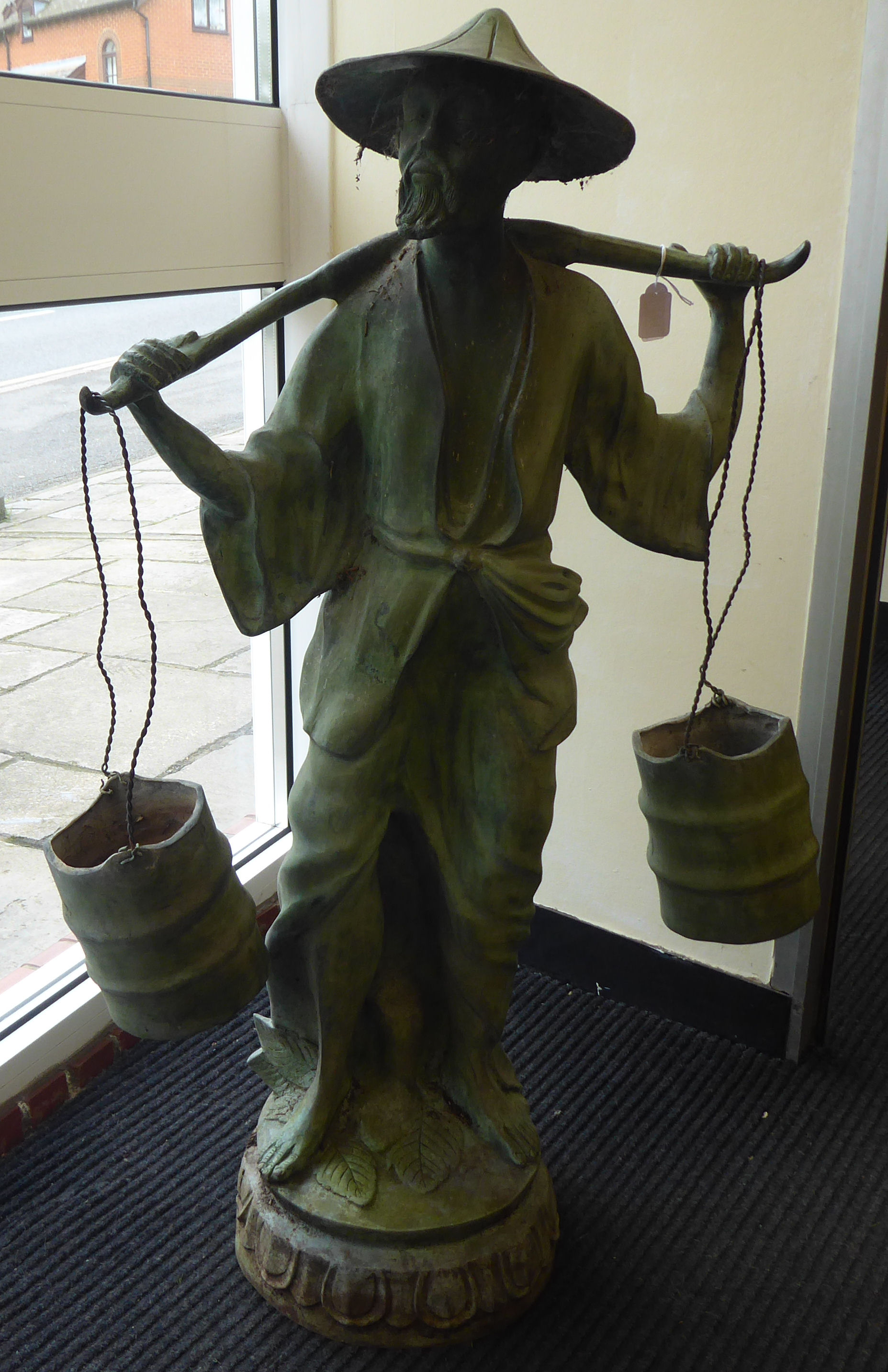 A 20thC cast and patinated green bronze standing Asian artisan figure, a bearded man, carrying two