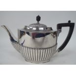 A late Victorian silver teapot of oval, demi-reeded form with a swept spout, hinged lid, ebonised