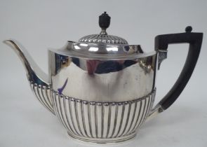 A late Victorian silver teapot of oval, demi-reeded form with a swept spout, hinged lid, ebonised