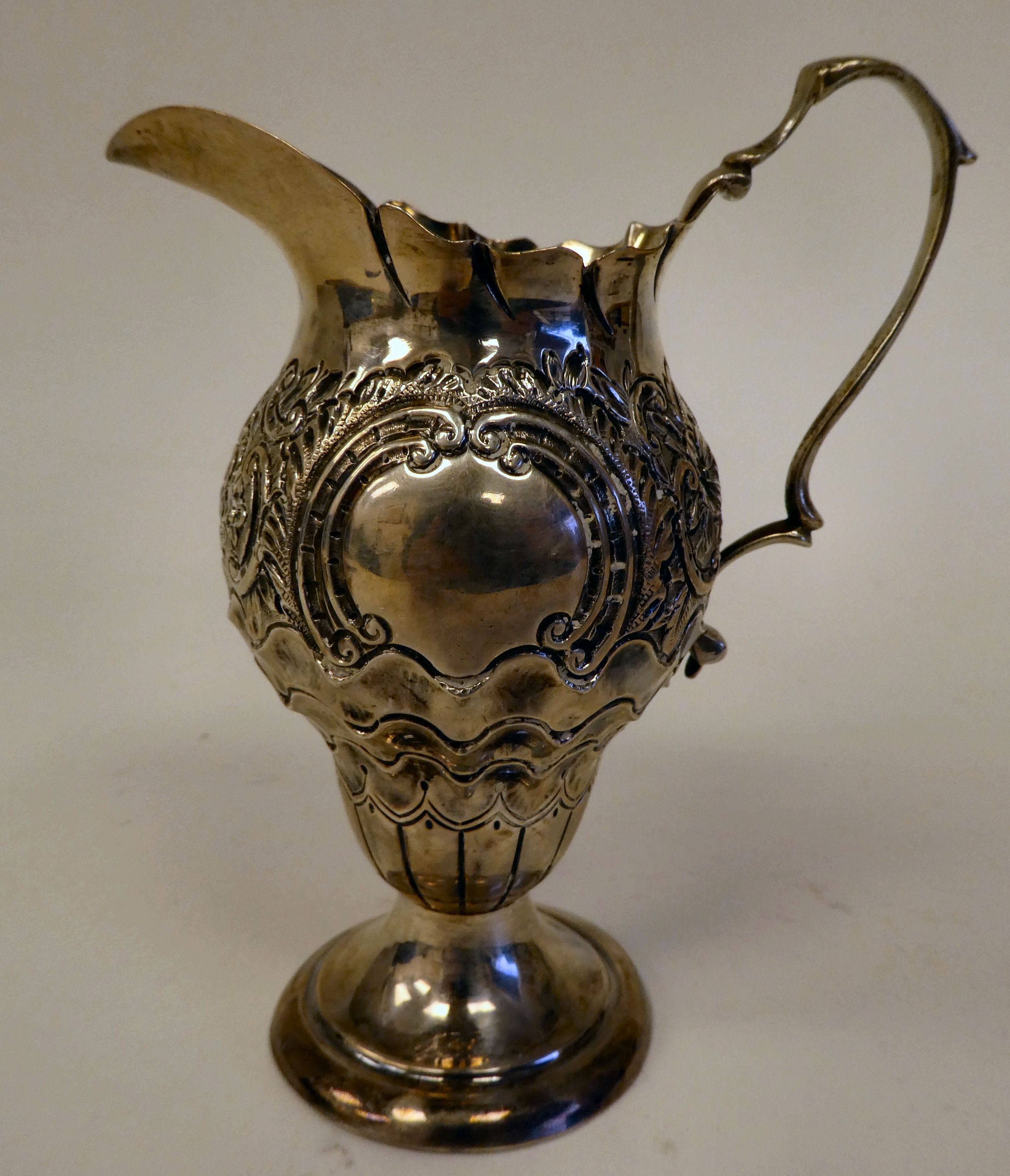 A late Victorian silver pedestal cream jug of pear form with a double C-scrolled handle, scaled,