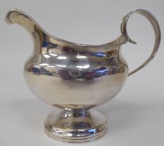 A silver pedestal cream jug of squat, bulbous form with an applied wire rim and C-scrolled