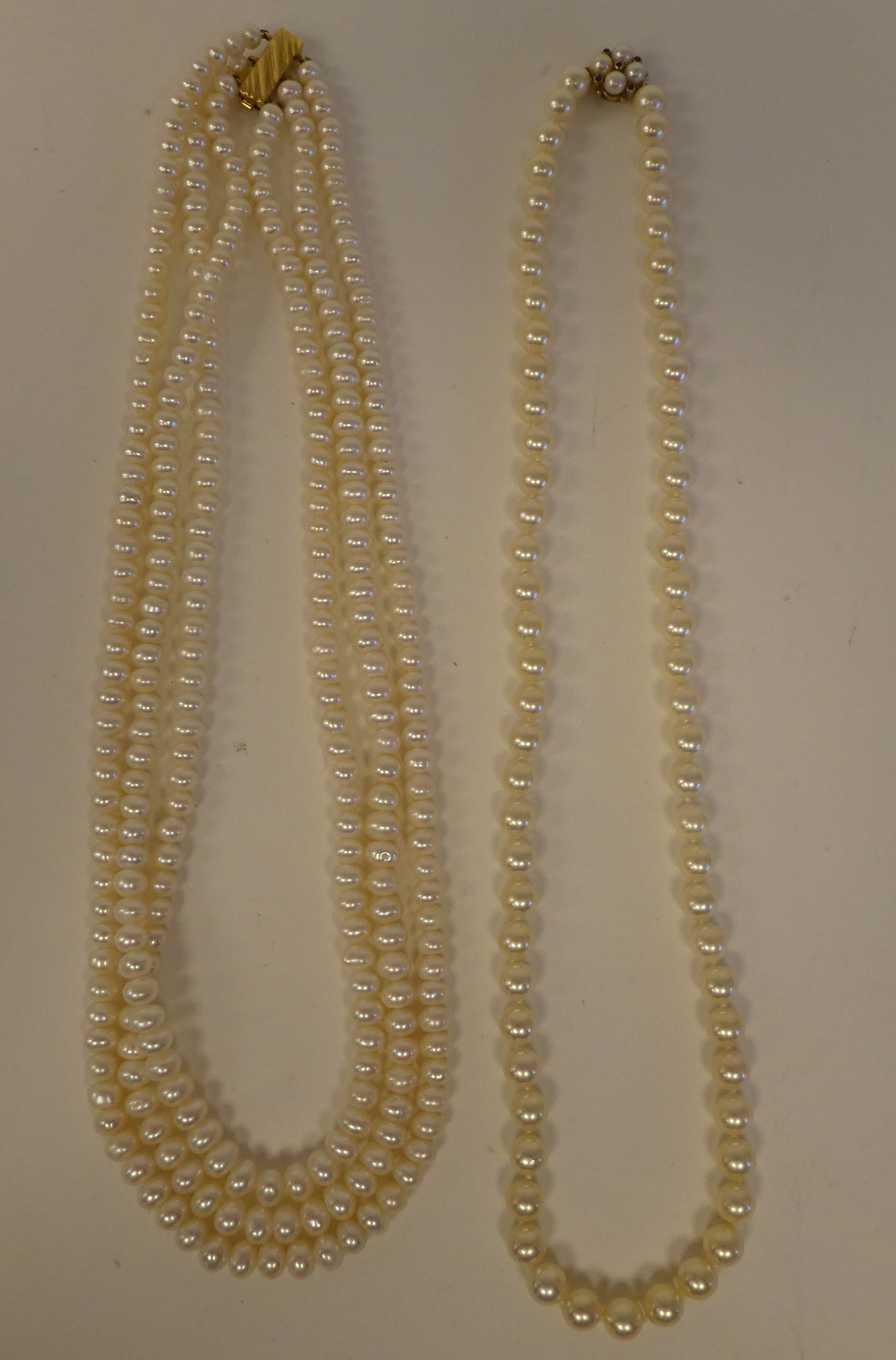 A triple string pearl necklace; and another single strand example, both on 9ct gold clasps