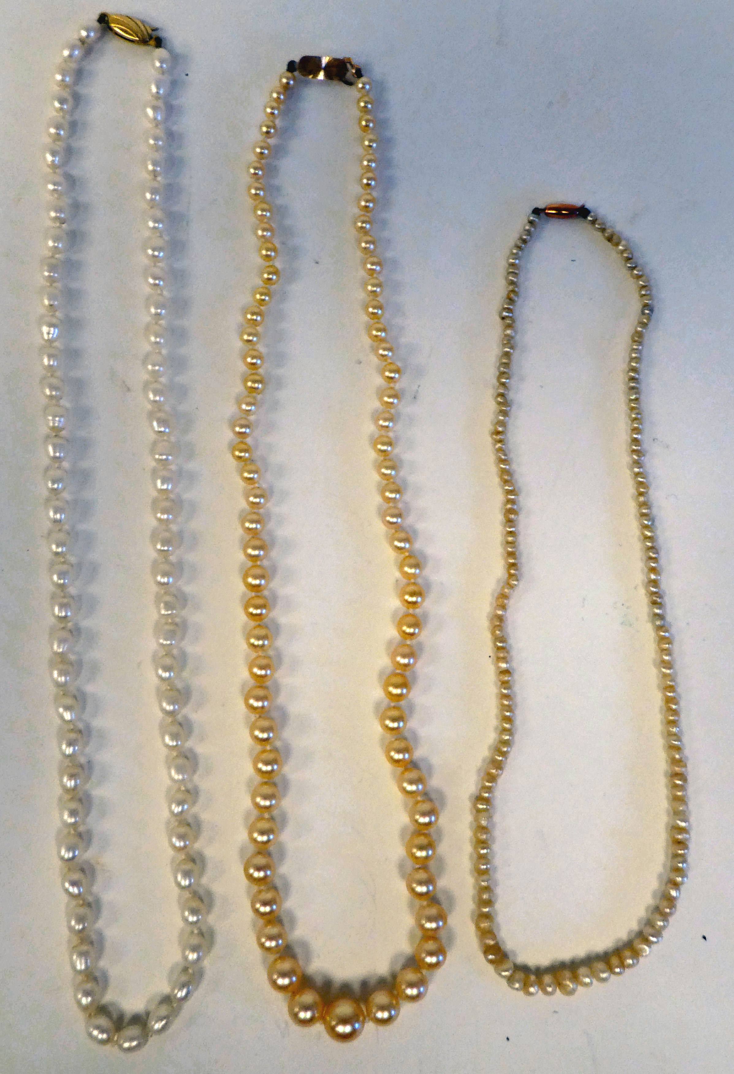 Three single strand pearl necklaces, each on a yellow metal clasp