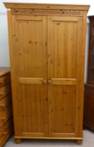 A modern honey coloured pine, two door wardrobe, enclosing a single shelf over a hanging rail, on