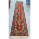A Super Keshan machine made runner, decorated with repeating designs, on a red ground  27" x 144"