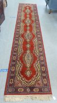 A Super Keshan machine made runner, decorated with repeating designs, on a red ground  27" x 144"