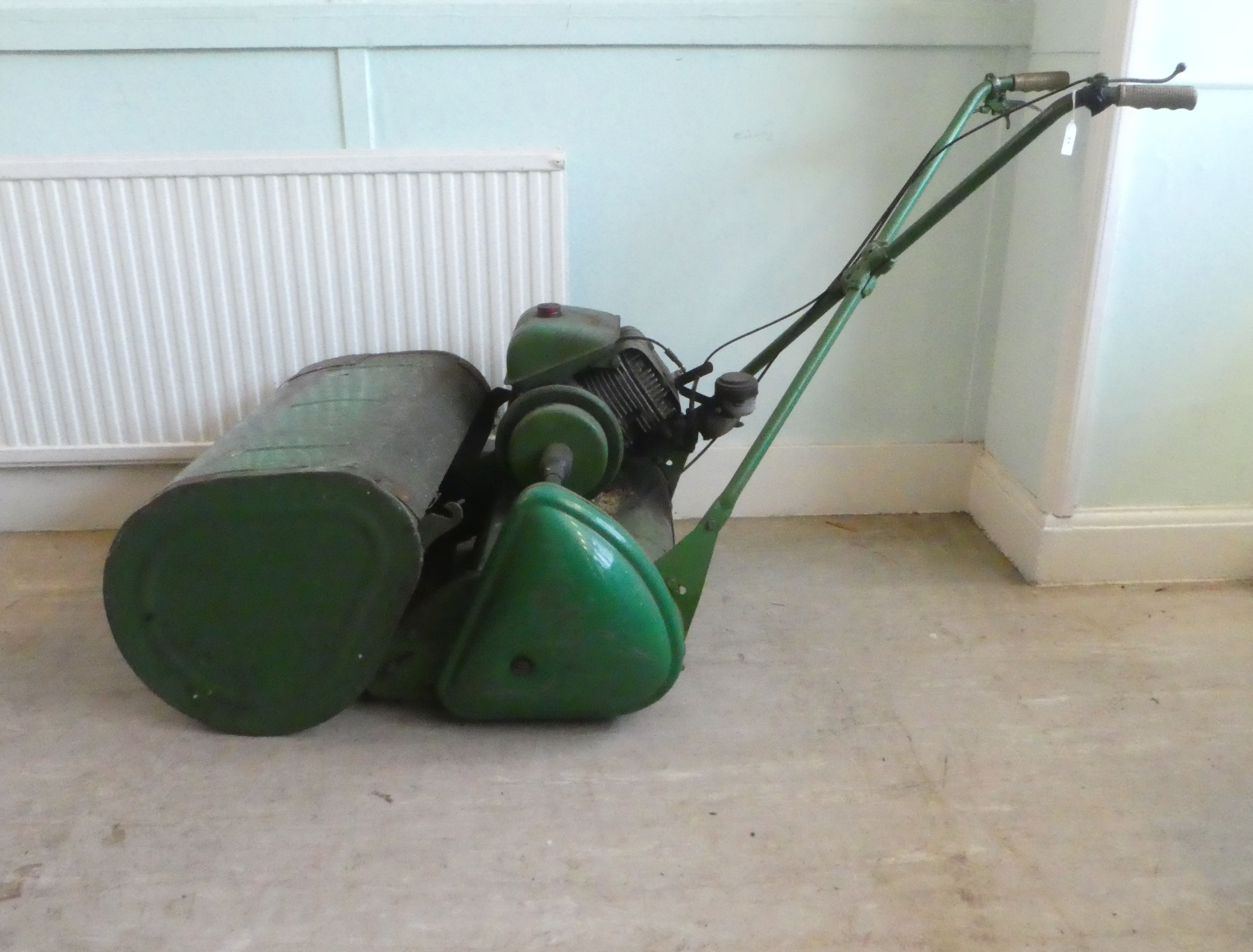 A vintage petrol driven cylindrical lawn mower with a grass box