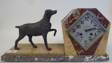 An Art Deco multi-coloured marble cased mantel clock, surmounted by a spelter standing hound; the