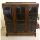 A 1930s oak display cabinet with three partially glazed doors, on a plinth and bun feet  49"h  45"w