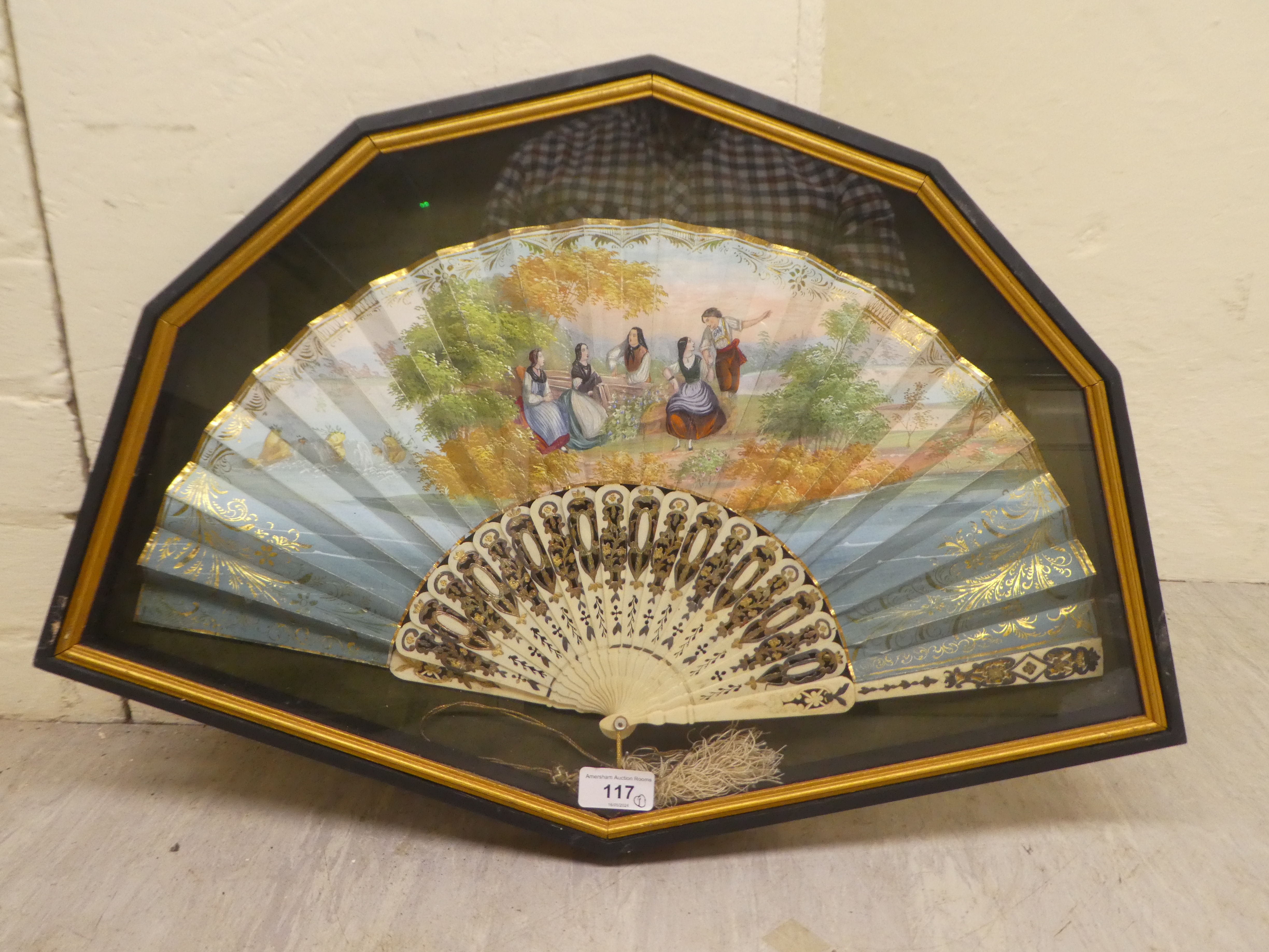 An early 20thC fan, decorated with figures in conversation, on bone spines, in a glazed box frame