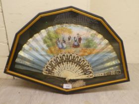 An early 20thC fan, decorated with figures in conversation, on bone spines, in a glazed box frame