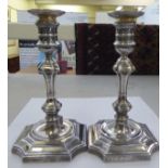 A pair of Georgian style loaded silver candlesticks of square outline, the knopped stems on incurved